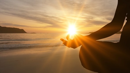 Entspannte Frau im Meditationsitz genießt den Sonnenaufgang am Meer